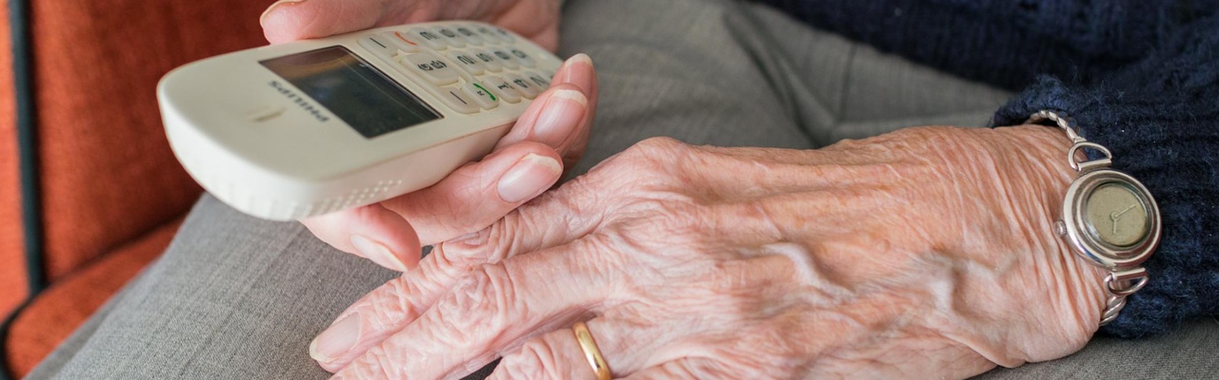 Een tachtig plusser houdt zijn telefoon vast en is klaar om te bellen.