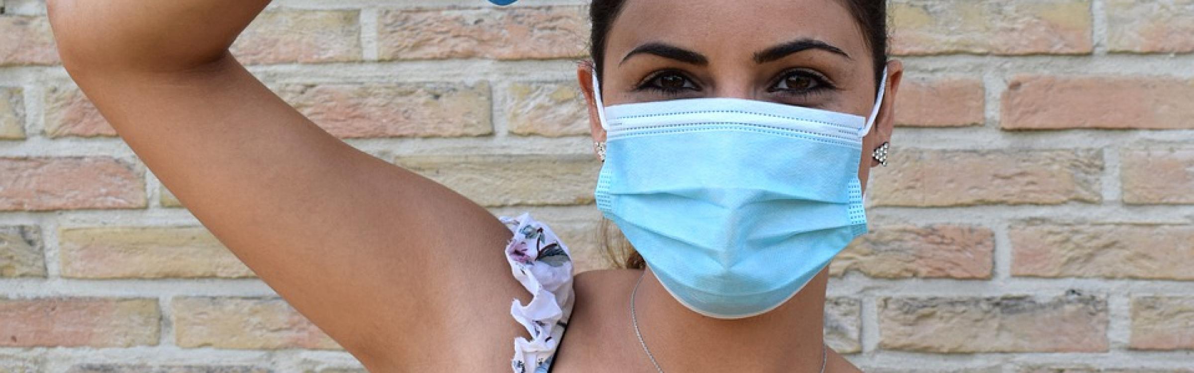 Een vrouw steekt haar arm in de lucht en draagt een mondmasker.
