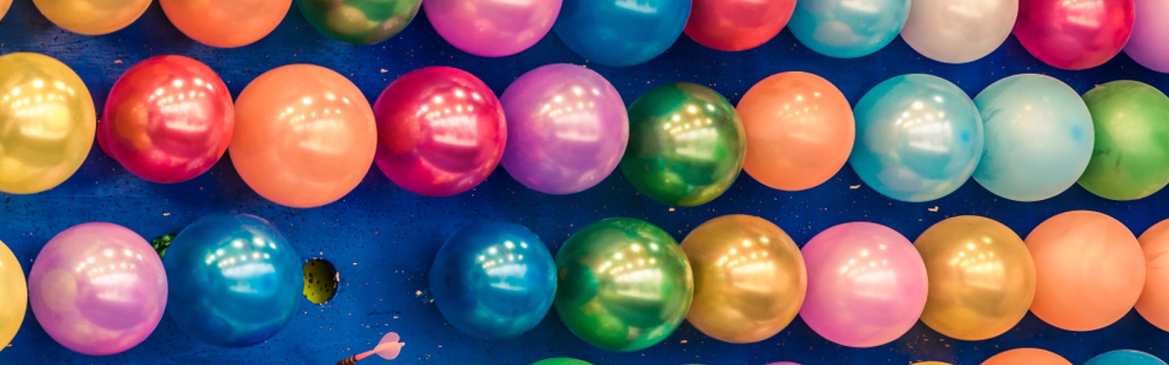 Allemaal kleine ballontjes hangen klaar in een kermiskraam om kapot geschoten te worden.