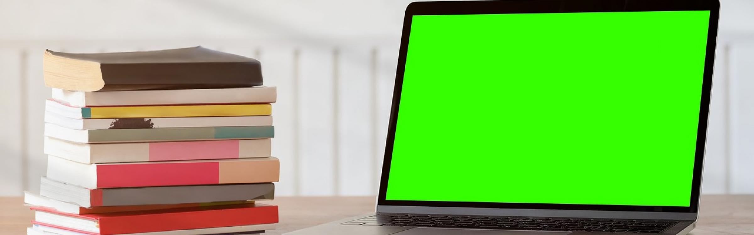 Een stapel boeken staan naast een computer.