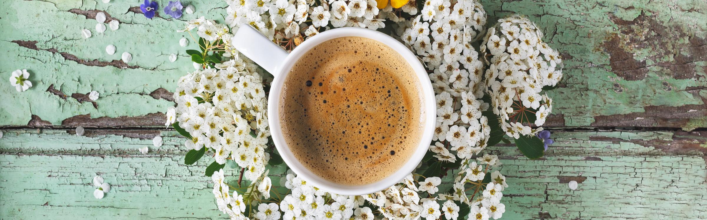 Een tas koffie staat op tafel omringd door bloemetjes.
