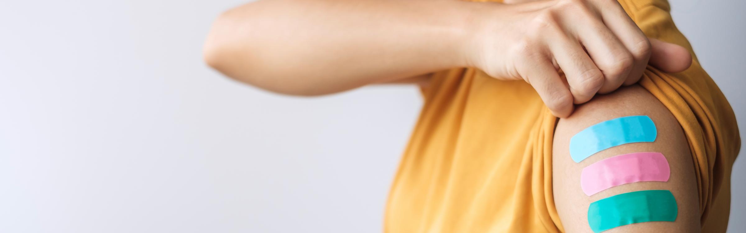 Een persoon laat haar arm zien met drie plakkers op door vaccinaties.