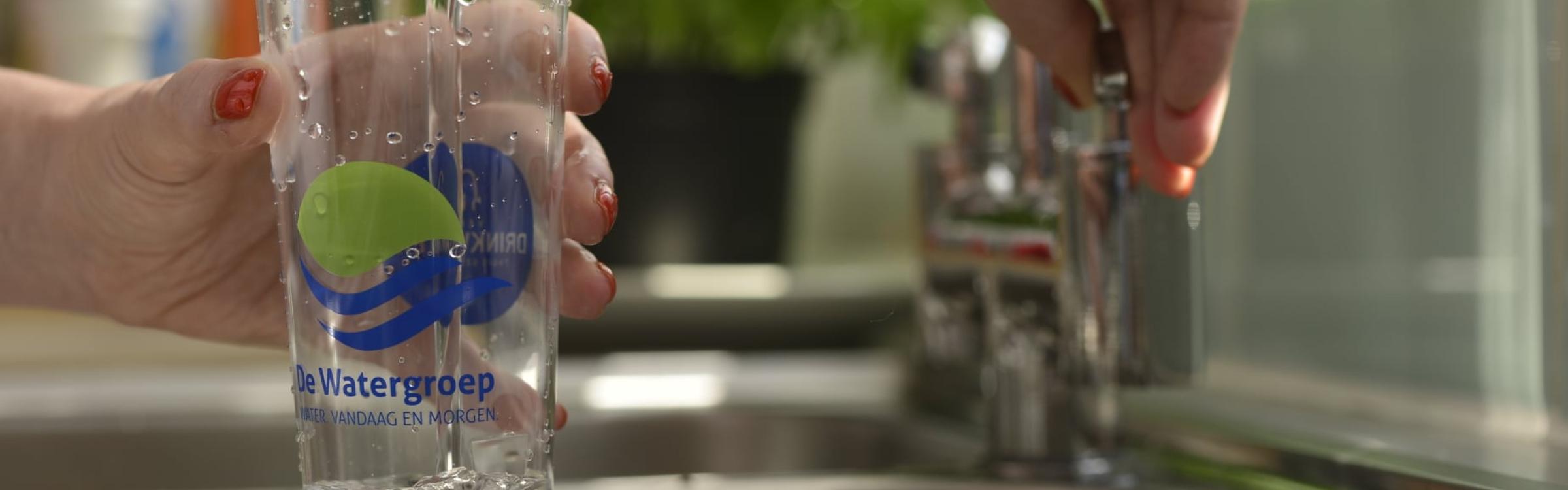 Een persoon pakt een glas water van de kraan.