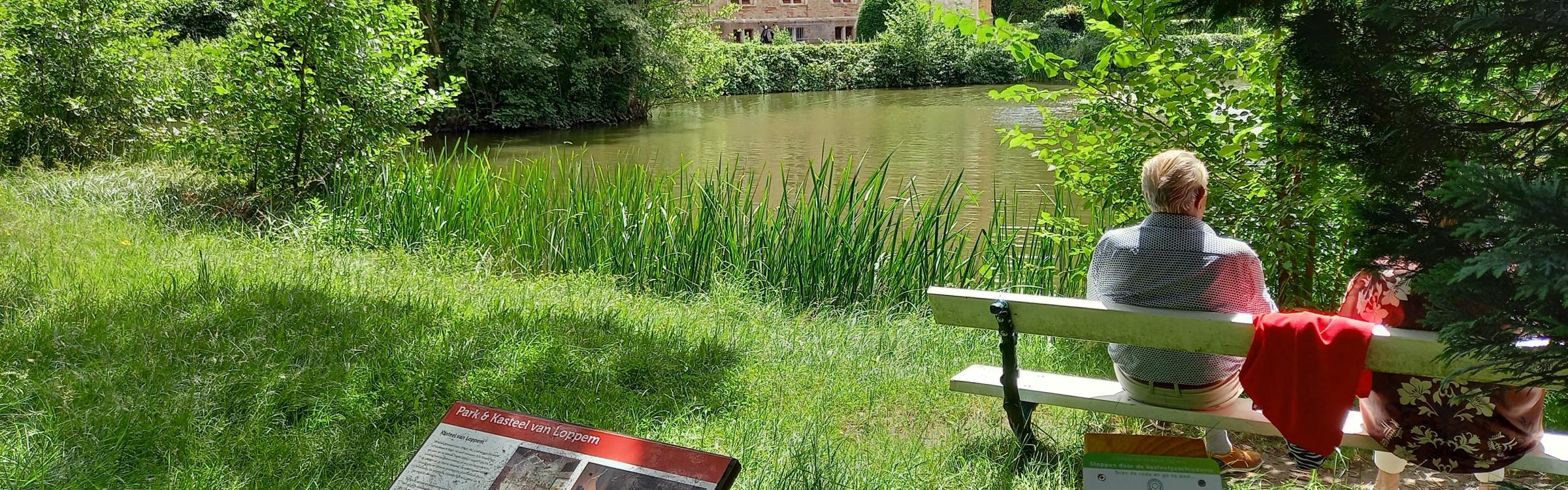 Persoon rust even uit op een bankje aan het Kasteel van Loppem