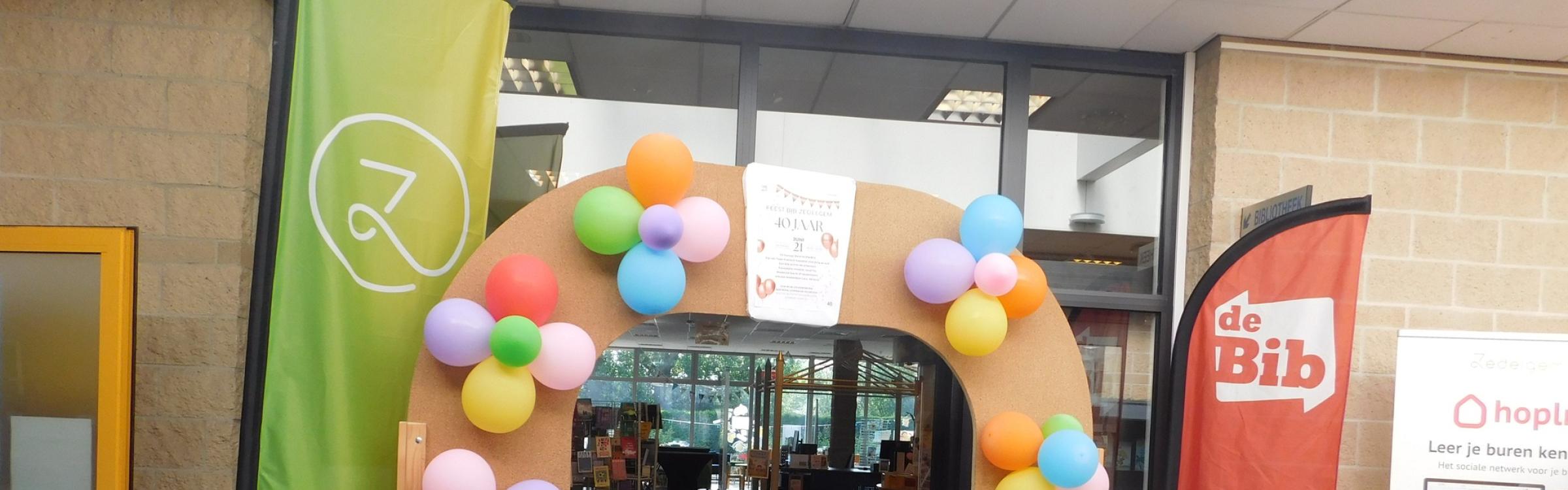 Foto van een houten boog, versierd met kleurrijke ballonnen voor 40 jaar bib Zedelgem.