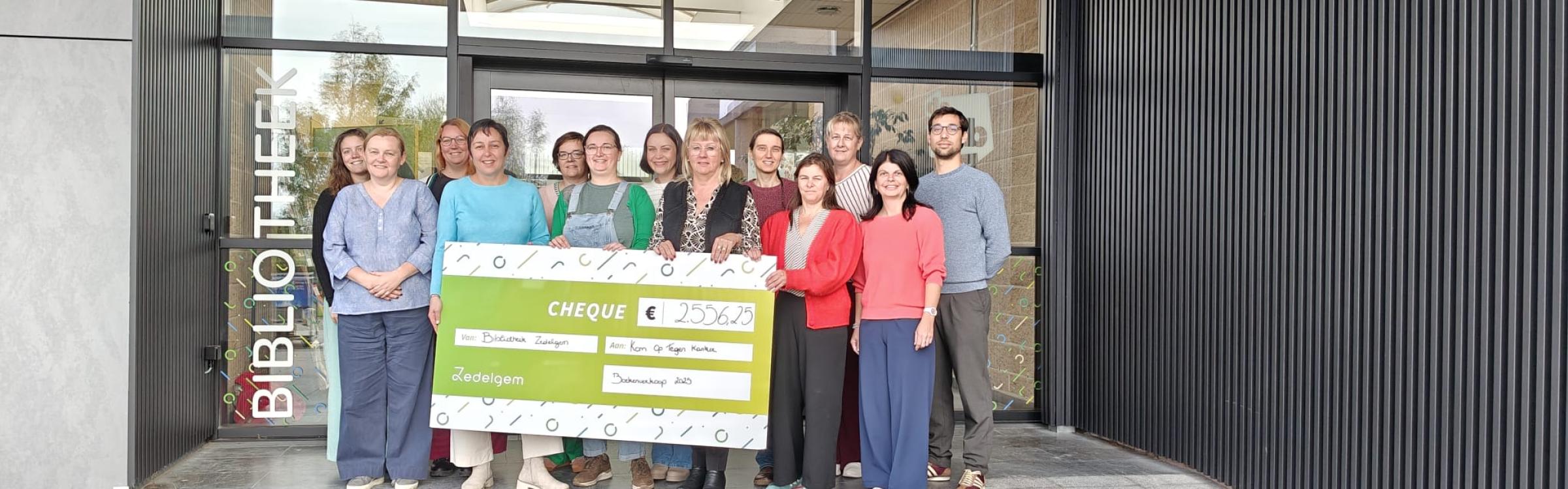 Medewerkers van de bib met burgemeester Annick Vermeulen en schepen van bib Soffie Pollet houden een checque vast met het opgehaalde bedrag van €2556,25 opgeschreven