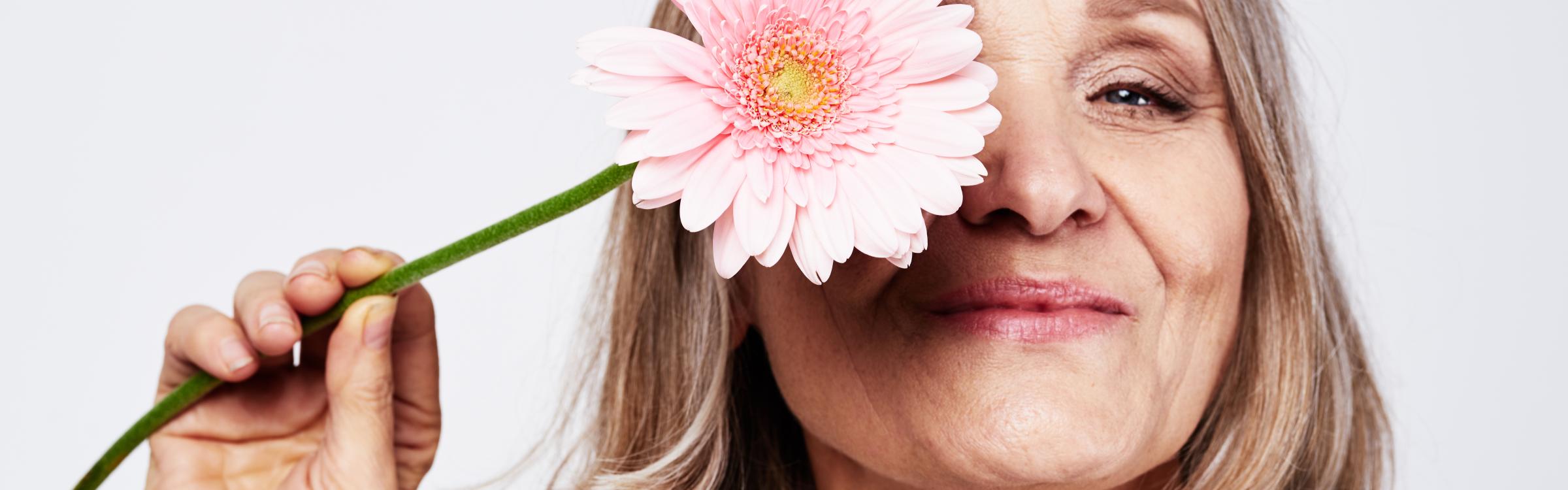 Oudere vrouw houdt een bloem voor haar gezicht