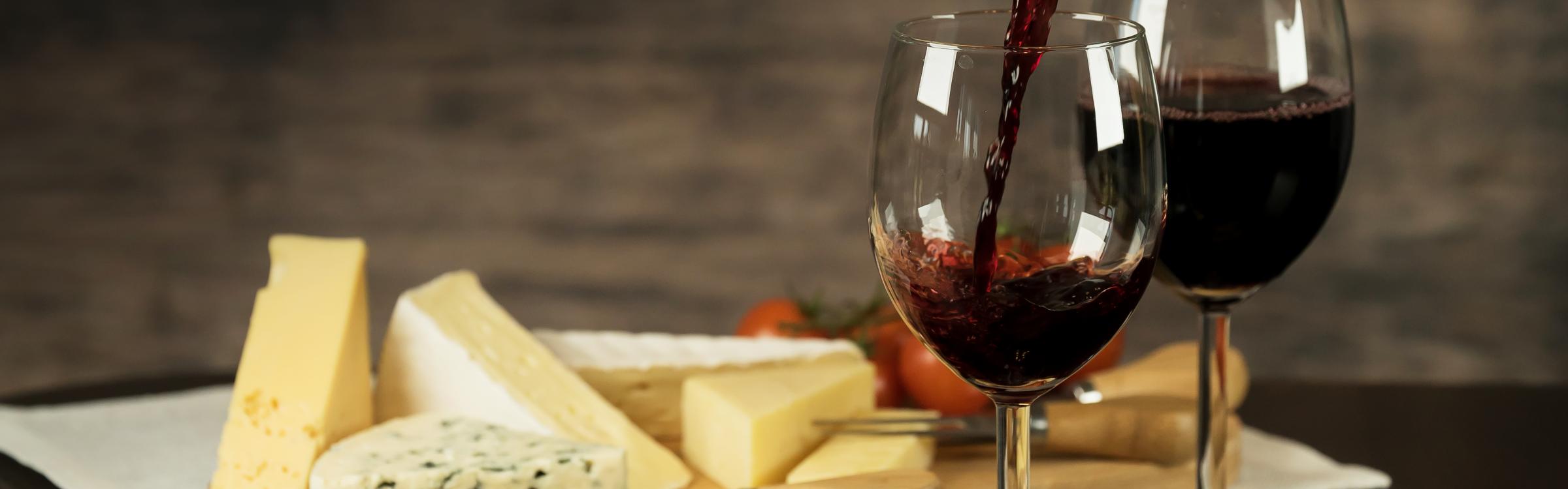 rode wijn wordt ingeschonken in een glas met op de achtergrond een kaasschotel
