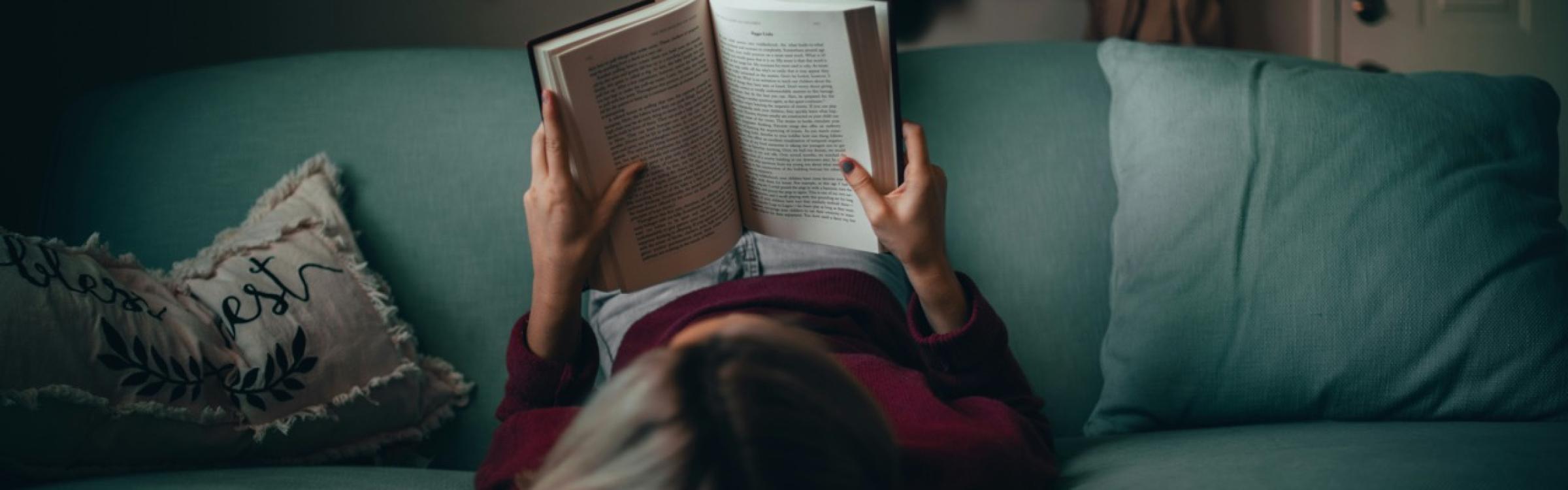 Vrouw leest een boek al liggend in een groene zetel