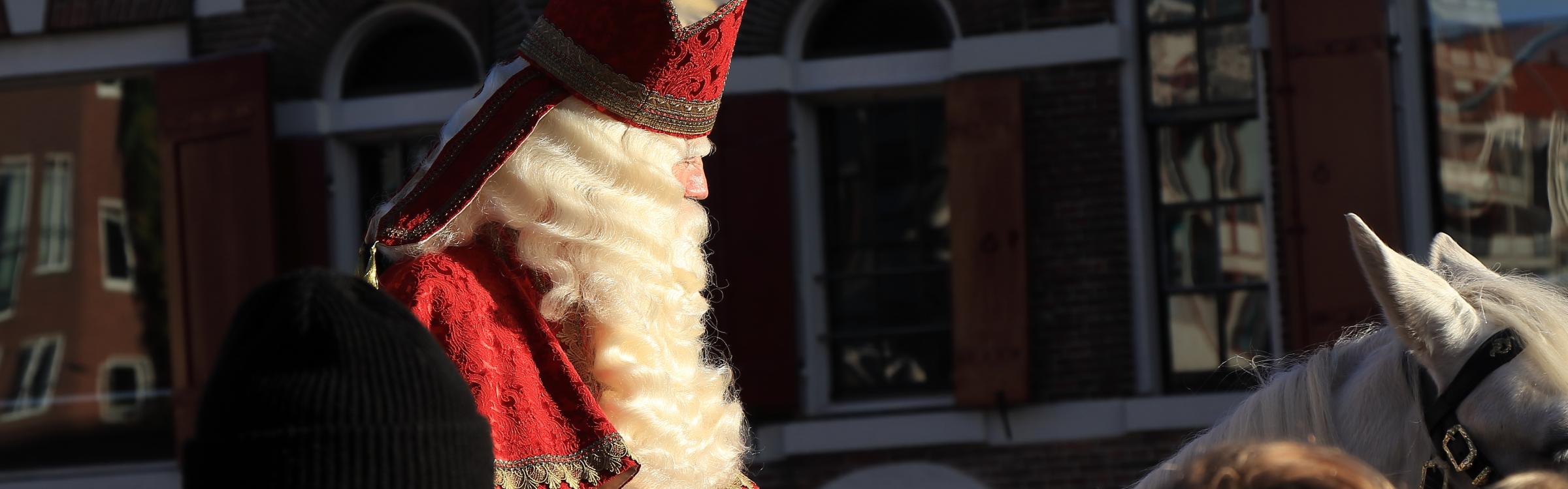 Sint rijdt op een wit paard door de straten en zwaait naar de mensen